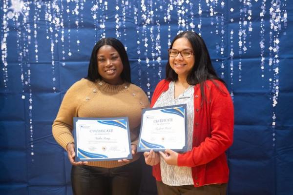 Photo of two girls holding certificates in front of a blue background. 