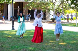 three Asian women dancing on lawn in traditional clothing