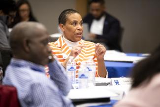 woman in orange blazer with white stripes sitting and talking at table