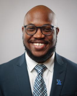 man in glasses, navy suit jacket and blue tie smiling for headshot