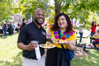 two individuals at a Latinx celebration and holding plates of food