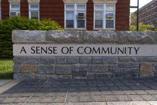 a low wall etched with the words "a sense of community" in the foreground; the background is a red brick building with windows.